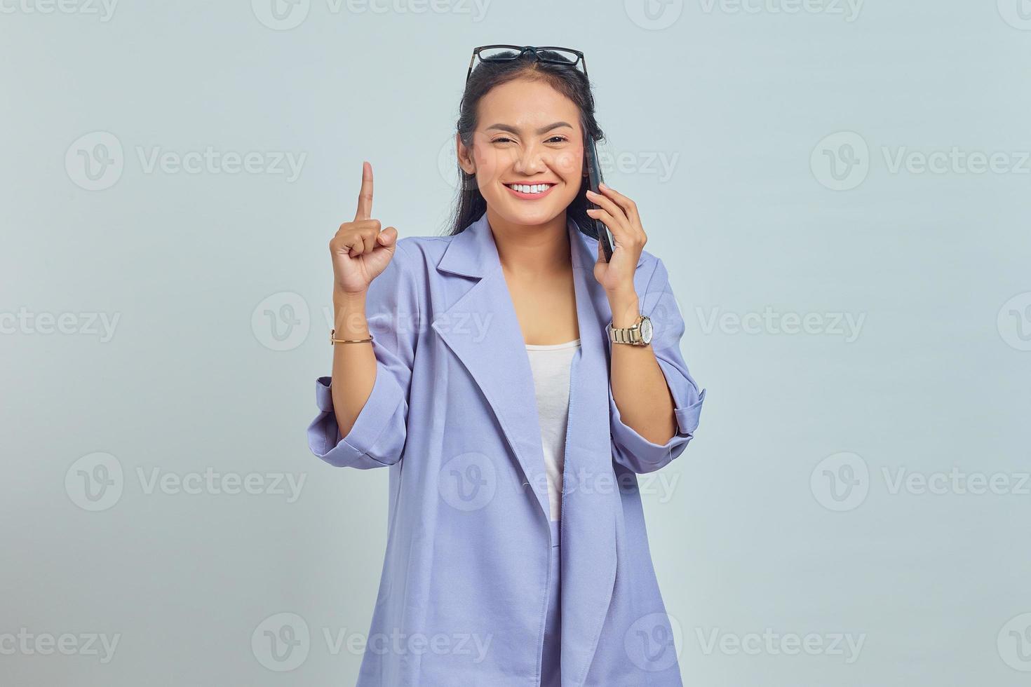 Portrait of happy young Asian woman talking on mobile phone and having an idea while pointing finger up isolated on white background photo