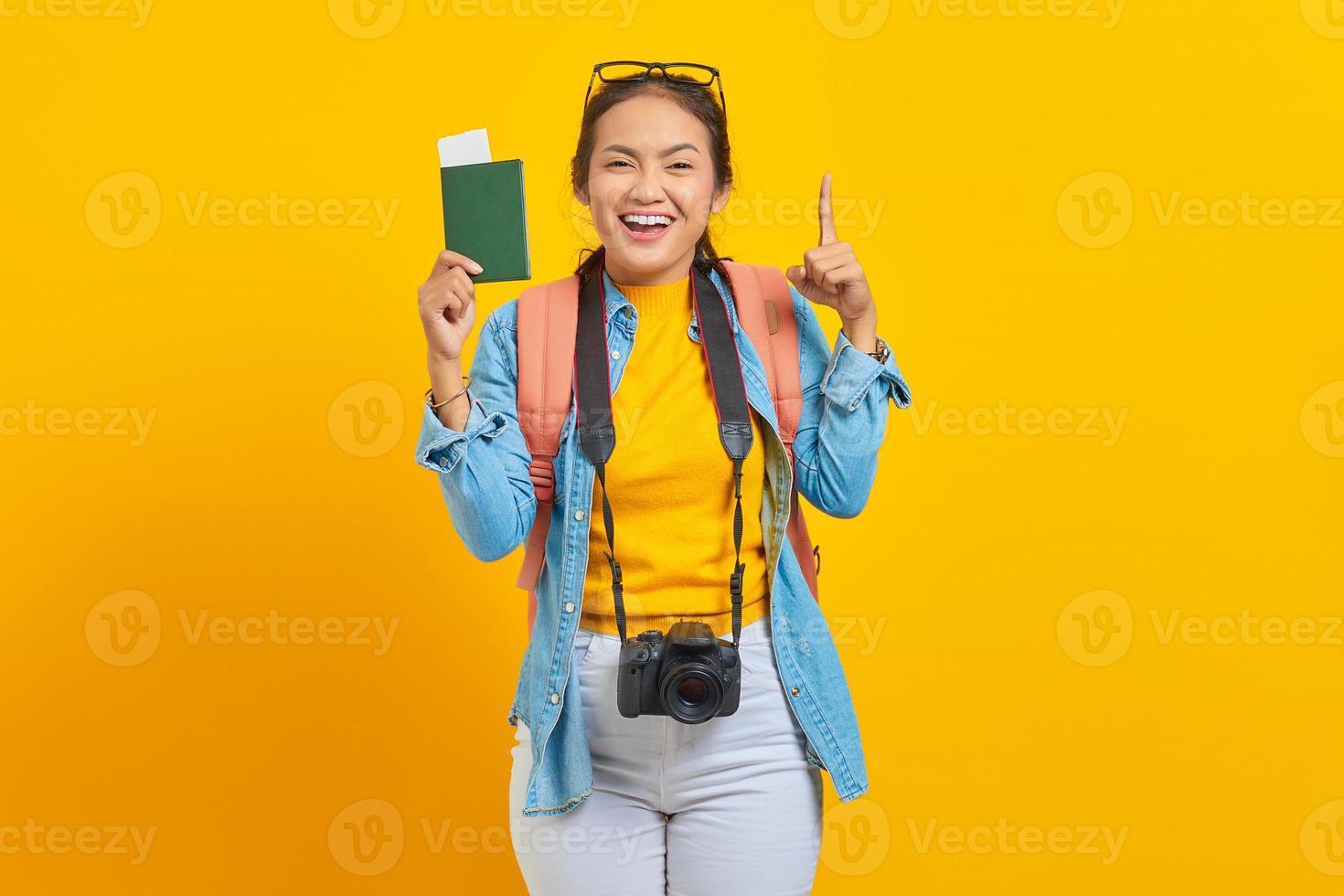 Portrait of cheerful young Asian traveler holding passport boarding pass ticket and pointing at copy space with fingers on yellow background. Passengers traveling on weekends.Air flight travel concept photo