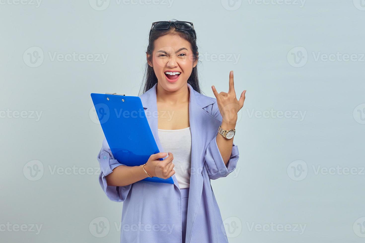 retrato de una joven y emocional mujer de negocios asiática con traje sosteniendo una carpeta de documentos y haciendo un cartel de rock and roll aislado en un fondo morado foto