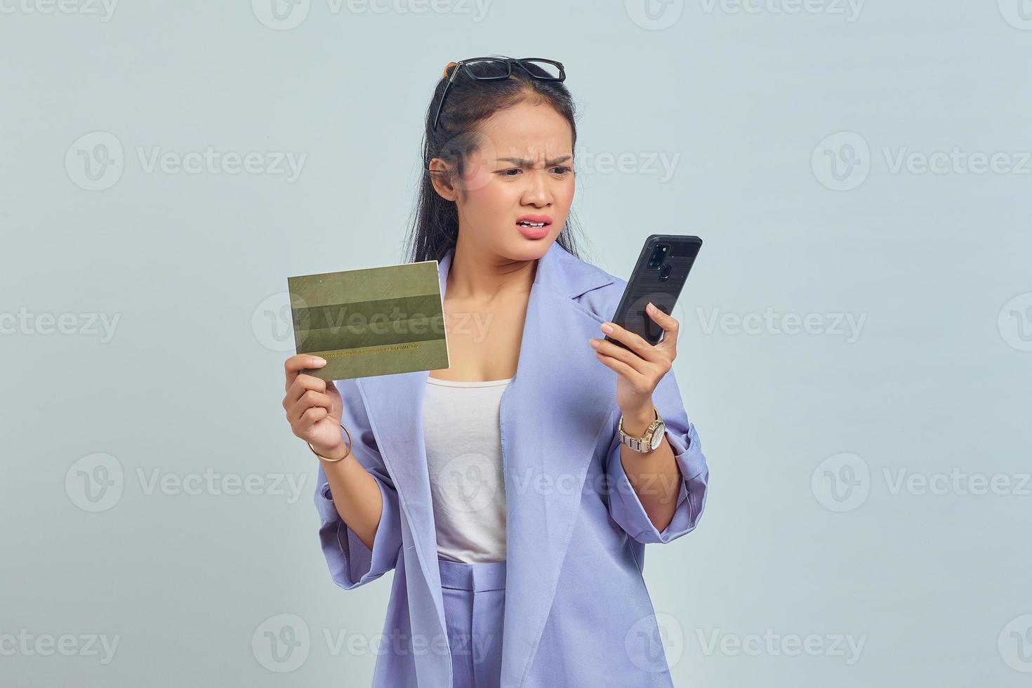 retrato de una joven asiática enojada que muestra el libro del vehículo y usa un teléfono inteligente aislado de fondo blanco foto