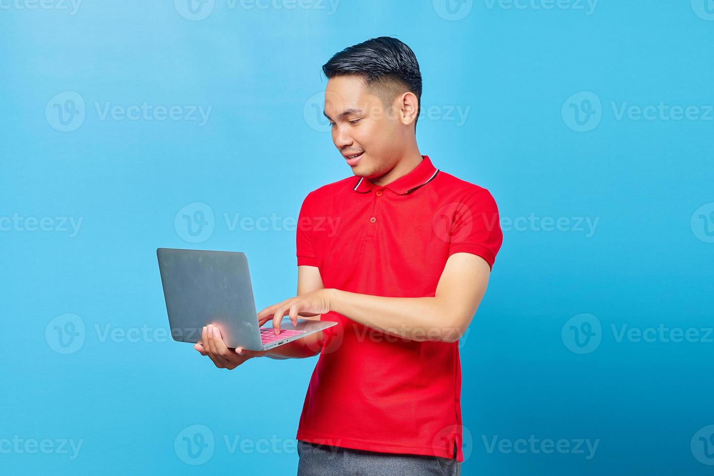 Portrait of smiling young handsome man holding and using a laptop on blue background photo