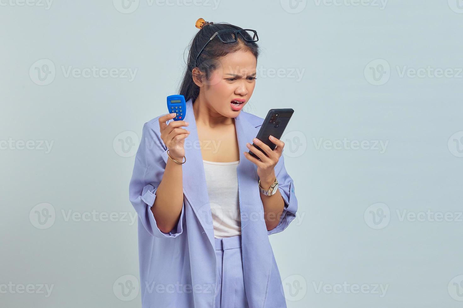Portrait of pensive young Asian woman holding banking token and holding smartphone over white background. concept money transfer via internet photo