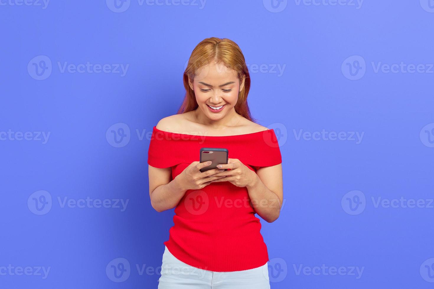 Portrait of positive young Asian woman smiling while holding cellphone isolated on purple background photo