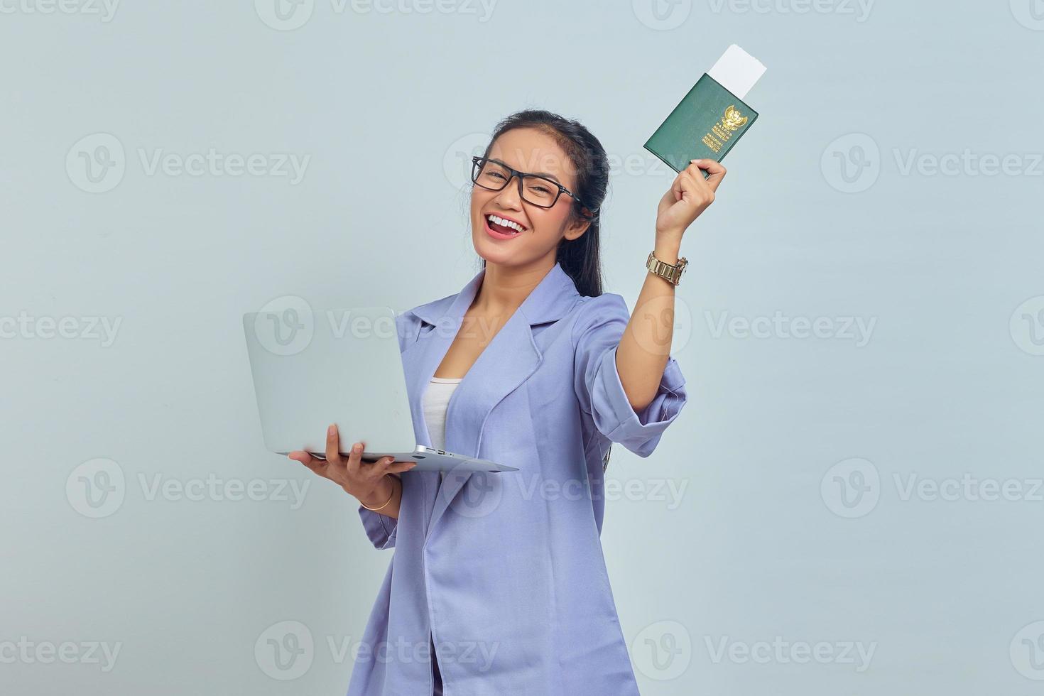 Portrait of young Asian woman standing using laptop and holding passport book with cheerful expression isolated on white background photo