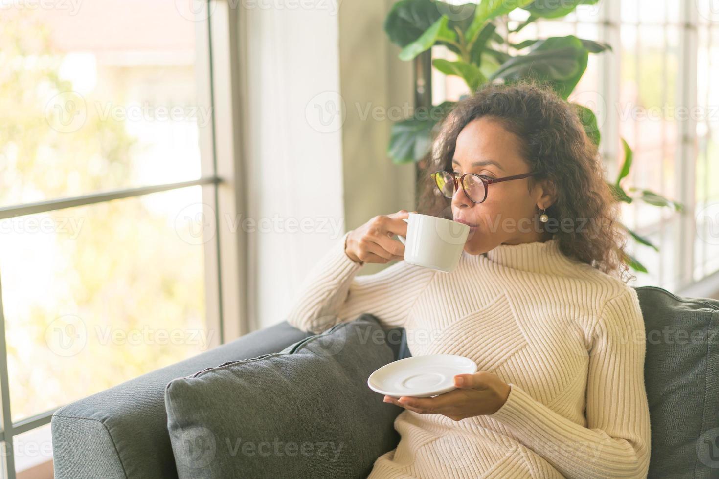 Mujer latina tomando café en el sofá en casa foto