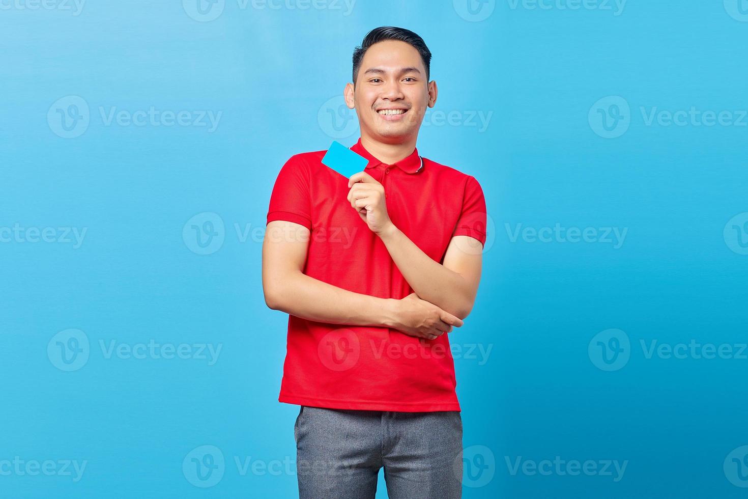 Portrait of cheerful Asian young man showing blank credit card and looking at camera isolated on blue background photo