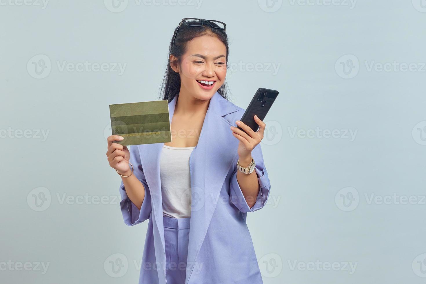 Portrait of cheerful young Asian woman showing vehicle book and using mobile phone isolated on white background photo