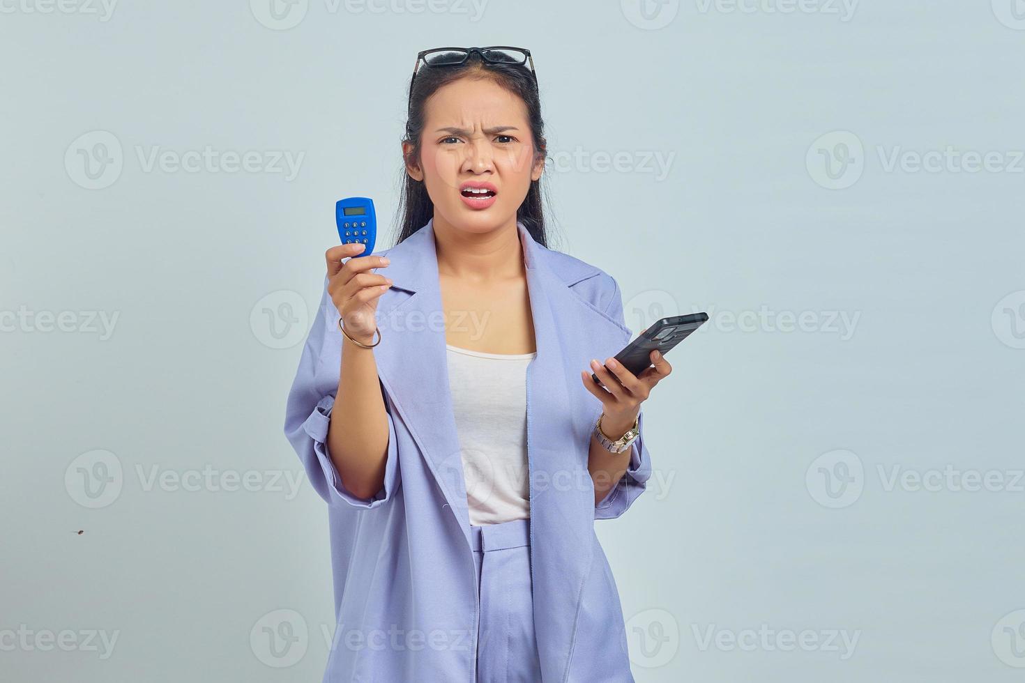 Portrait of surprised young Asian woman holding banking token and holding smartphone over white background. concept money transfer via internet photo