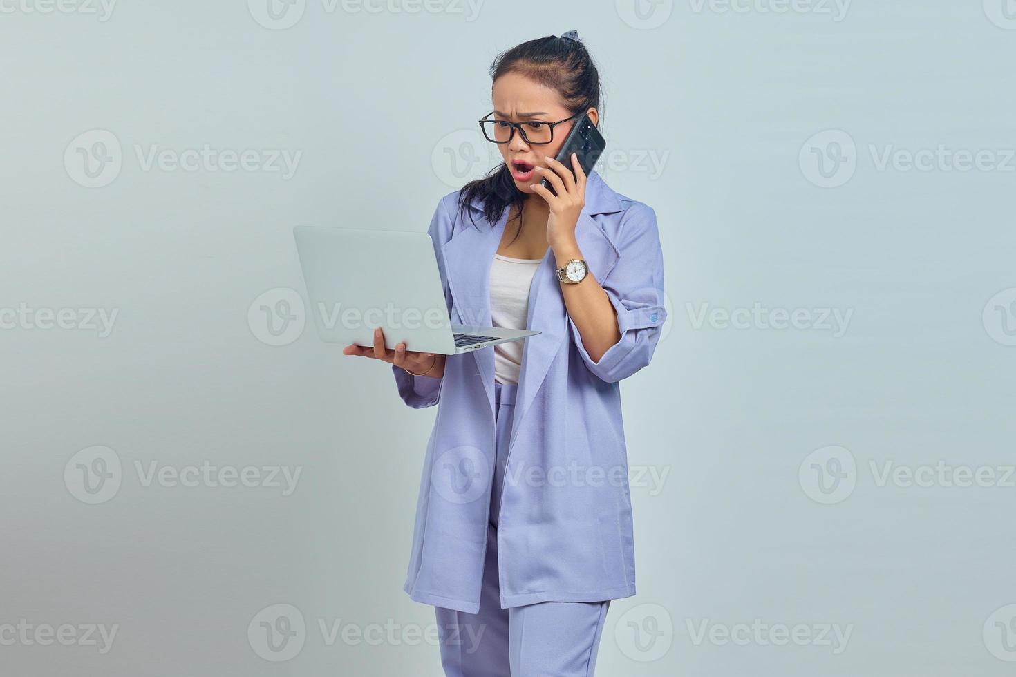 Portrait of surprised young Asian woman talking on mobile and looking at incoming email on laptop, confirmation of canceled job isolated on white background photo