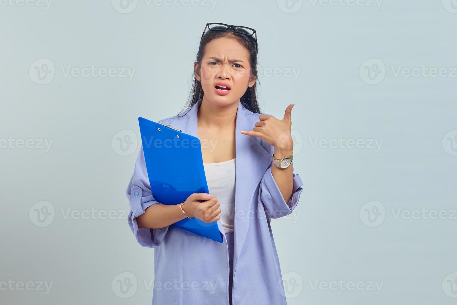 retrato de una joven asiática sorprendida con traje sosteniendo una carpeta de documentos y haciendo mi gesto de llamada aislado en un fondo morado foto