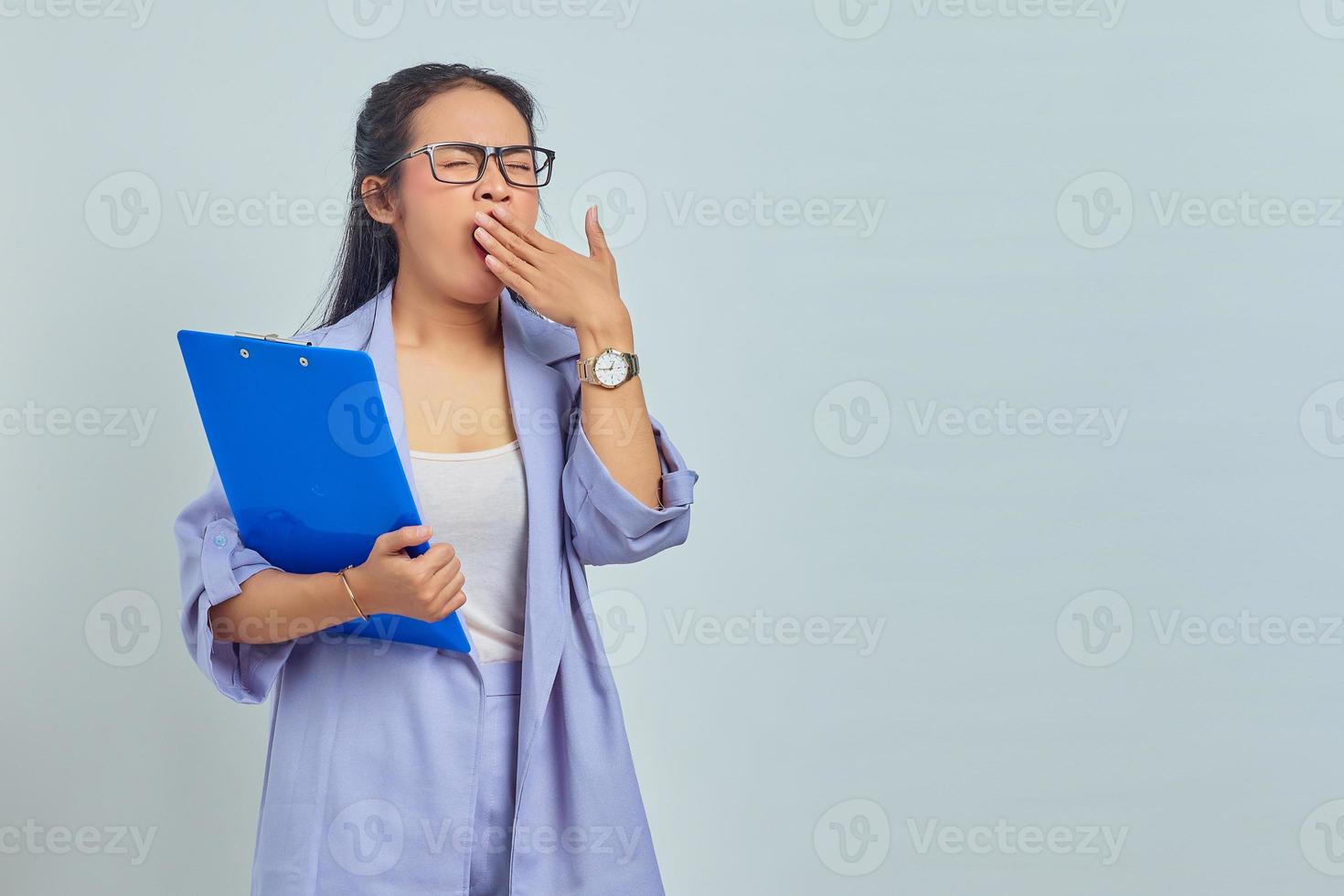 retrato de una hermosa joven asiática sosteniendo una carpeta de documentos mientras bostezaba con la boca queriendo dormir, con un problema de insomnio aislado en un fondo morado foto