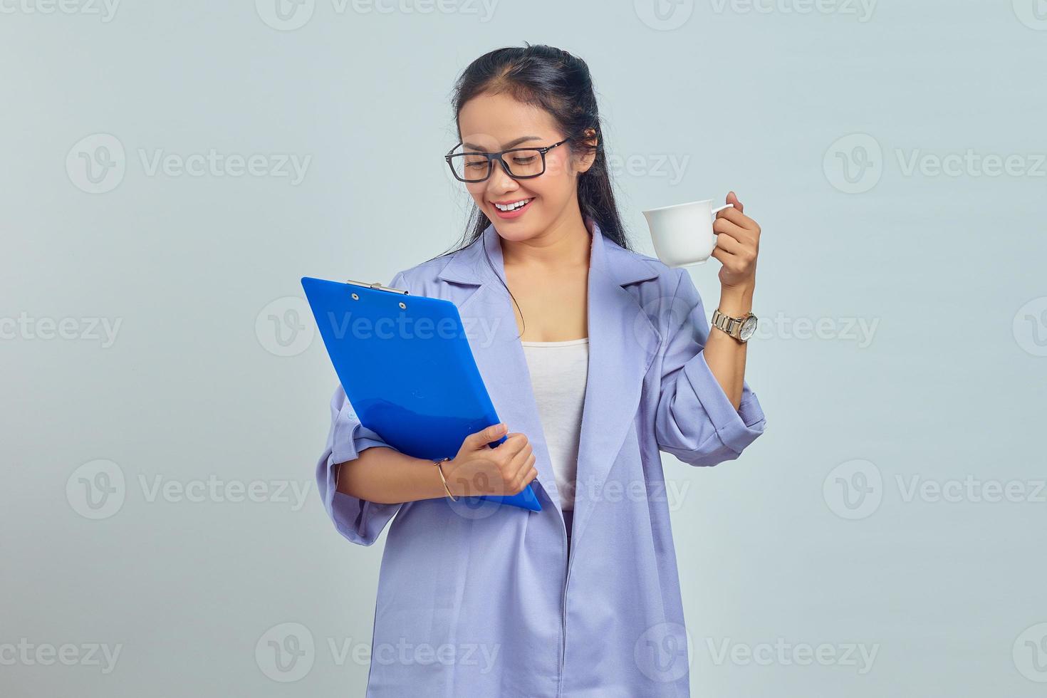 retrato de una joven empresaria asiática sonriente con traje sosteniendo una carpeta de documentos y sosteniendo una taza aislada en un fondo morado foto