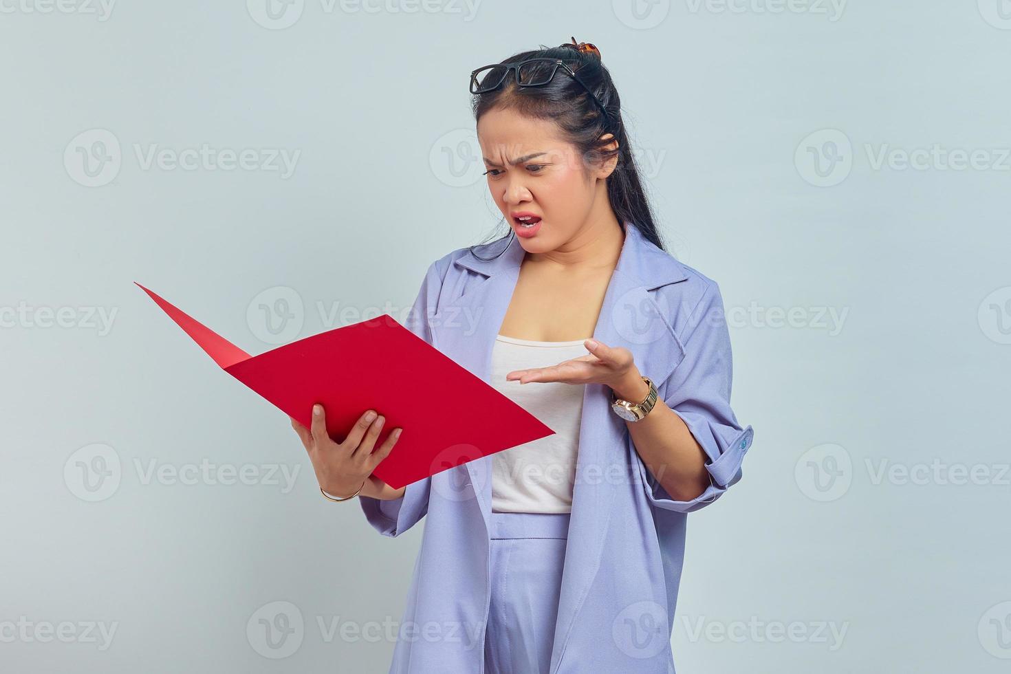 retrato de una joven empresaria asiática enfadada con traje de pie apuntando a la carpeta de documentos con las palmas aisladas en un fondo morado foto