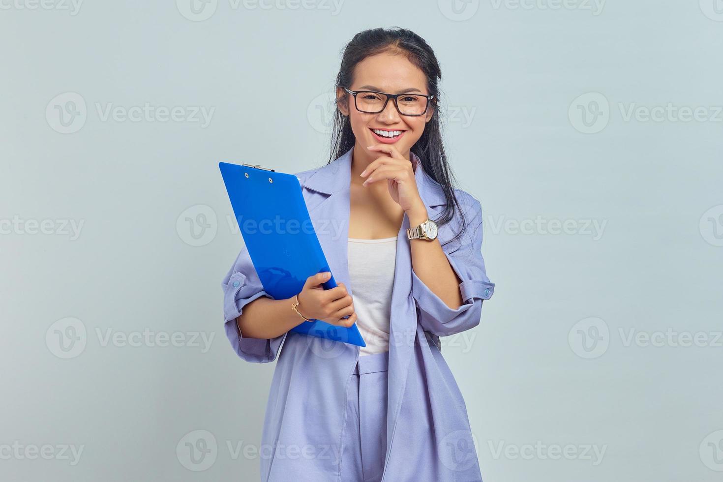 retrato de una joven y alegre mujer de negocios asiática sosteniendo la barbilla mientras sostenía una carpeta de documentos aislada en un fondo morado foto