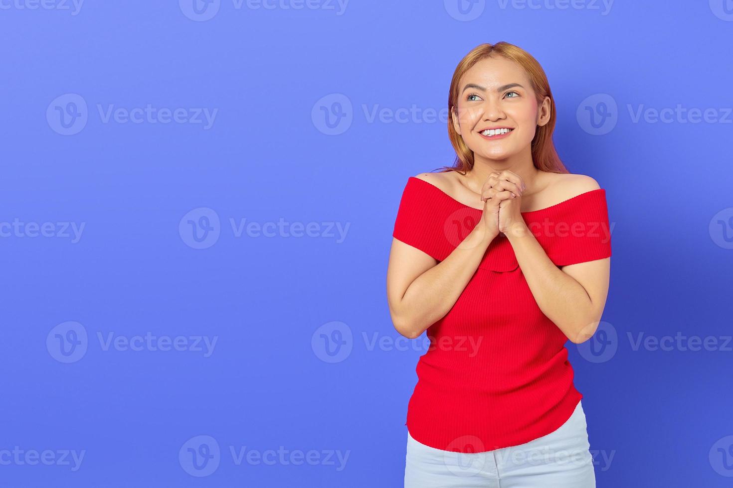 Smiling beautiful Asian woman in red dress rubbing hands and looking confident isolated over purple background photo