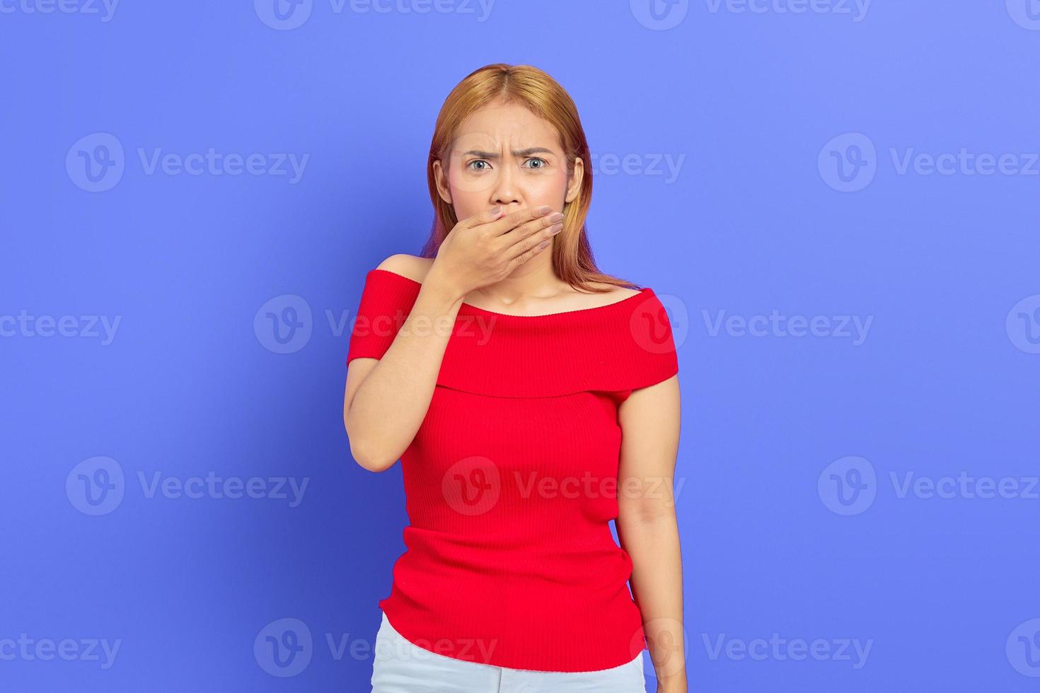 Portrait of shocked young Asian woman covering mouth with hand on purple background photo
