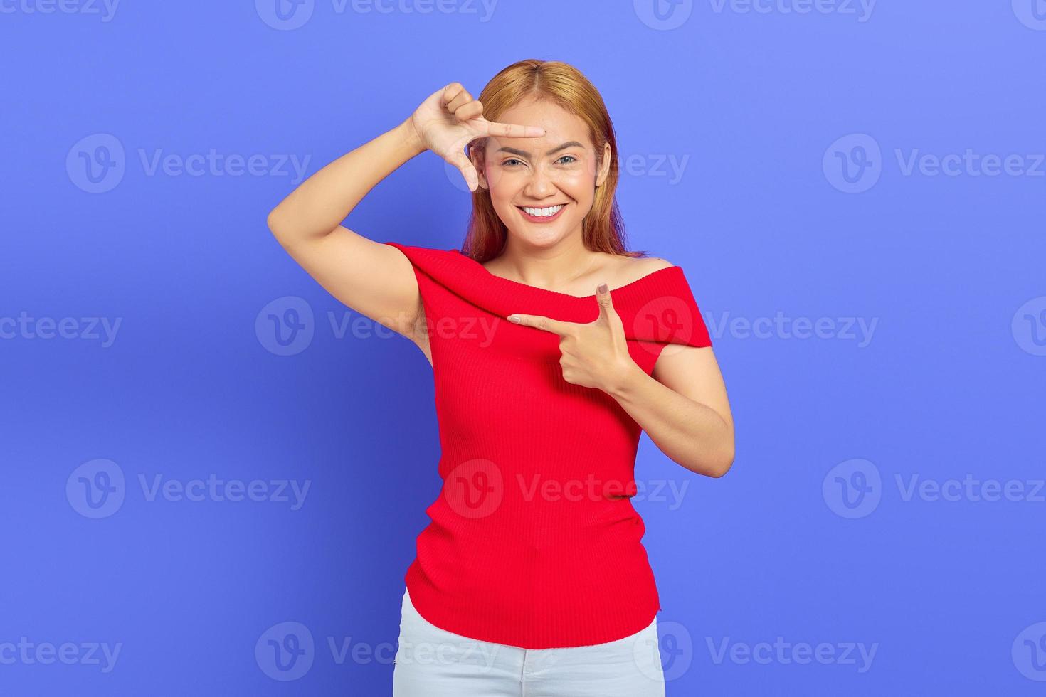 Portrait of smiling Asian woman making frame gesture with finger isolated on purple background photo