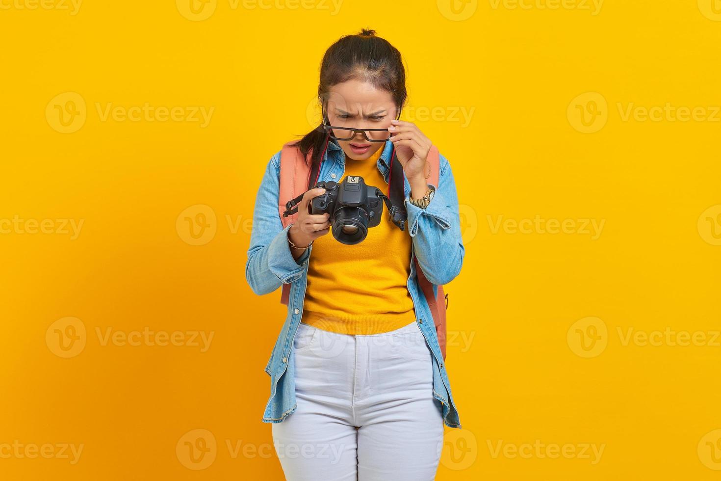 retrato de una joven asiática sorprendida mirando una foto en una cámara aislada de fondo amarillo. pasajero que viaja los fines de semana. concepto de viaje de vuelo aéreo