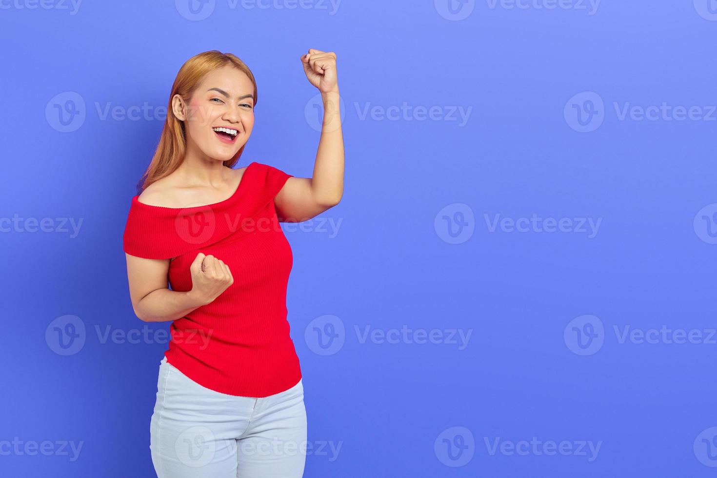 Cheerful young Asian woman celebrating victory, euphoric over achievement on purple background photo