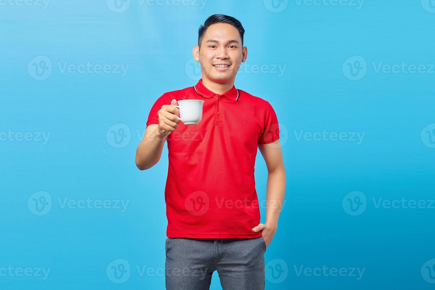 retrato de un apuesto joven asiático sonriente sosteniendo una taza de café aislado de fondo azul foto