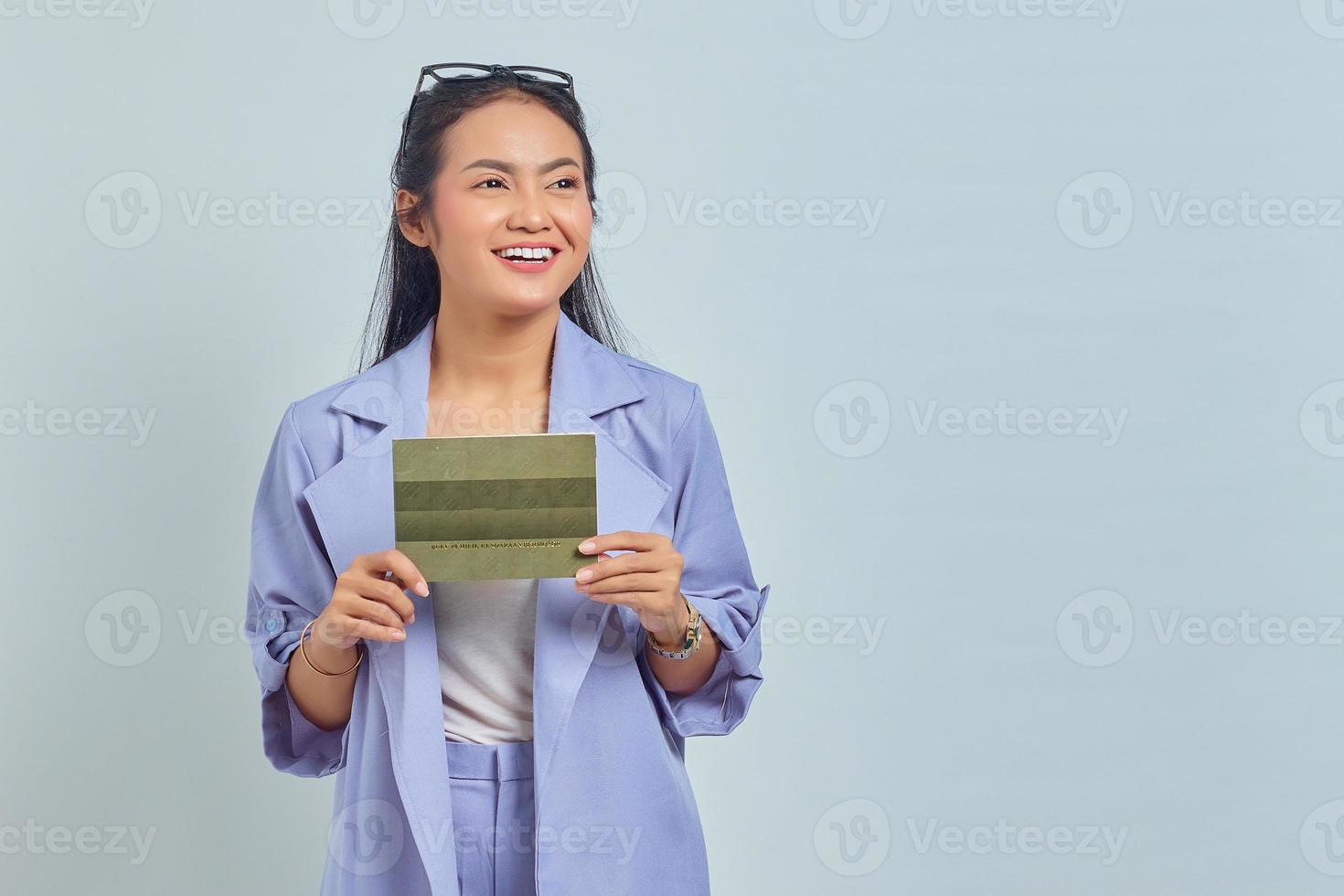 Portrait of smiling young Asian woman holding vehicle book in good mood and looking at empty space isolated on white background photo