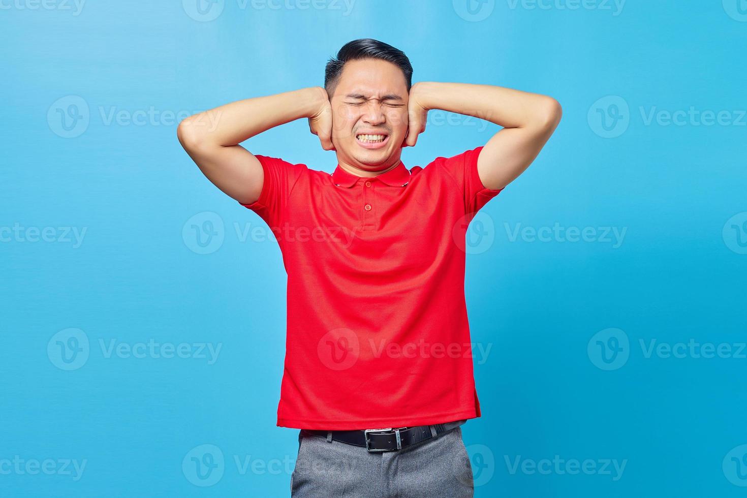 Portrait of frustrated Asian handsome young man covering ears with angry expression isolated on blue background photo