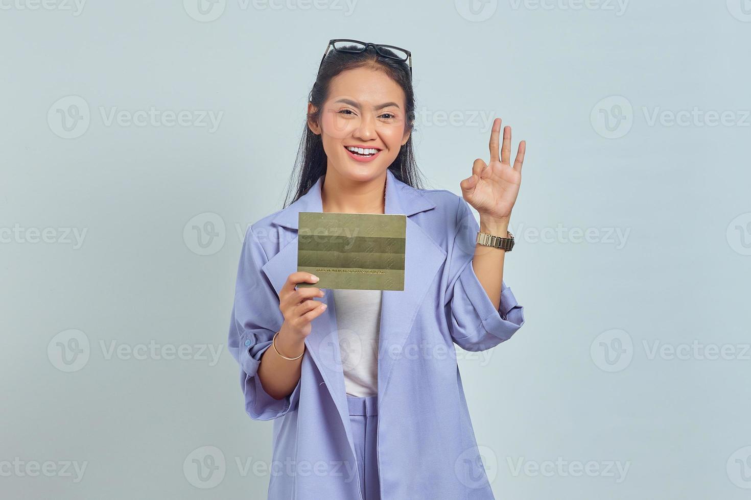 Portrait of smiling young Asian woman holding vehicle book and showing thumbs up gesture, Approving expression looking at camera showing success isolated on white background photo