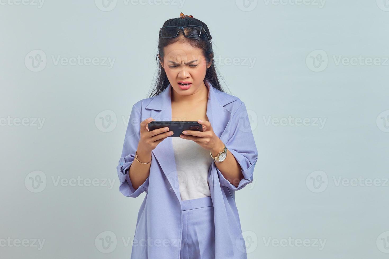 Portrait of angry young Asian woman playing game on mobile isolated on white background photo