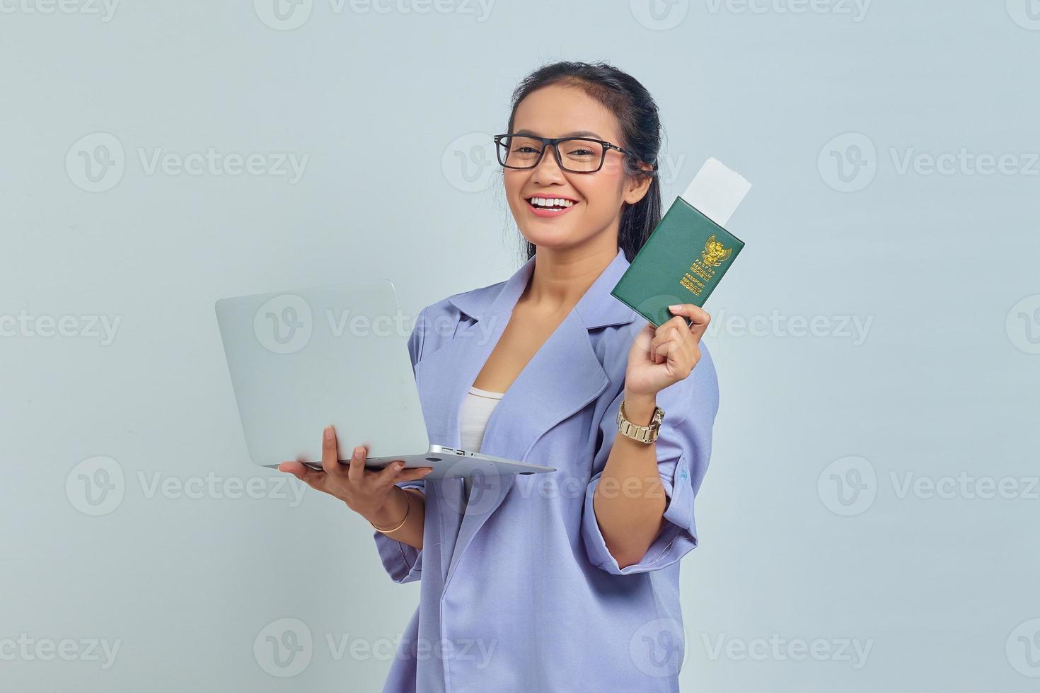 Portrait of young Asian woman standing using laptop and holding passport book with cheerful expression isolated on white background photo