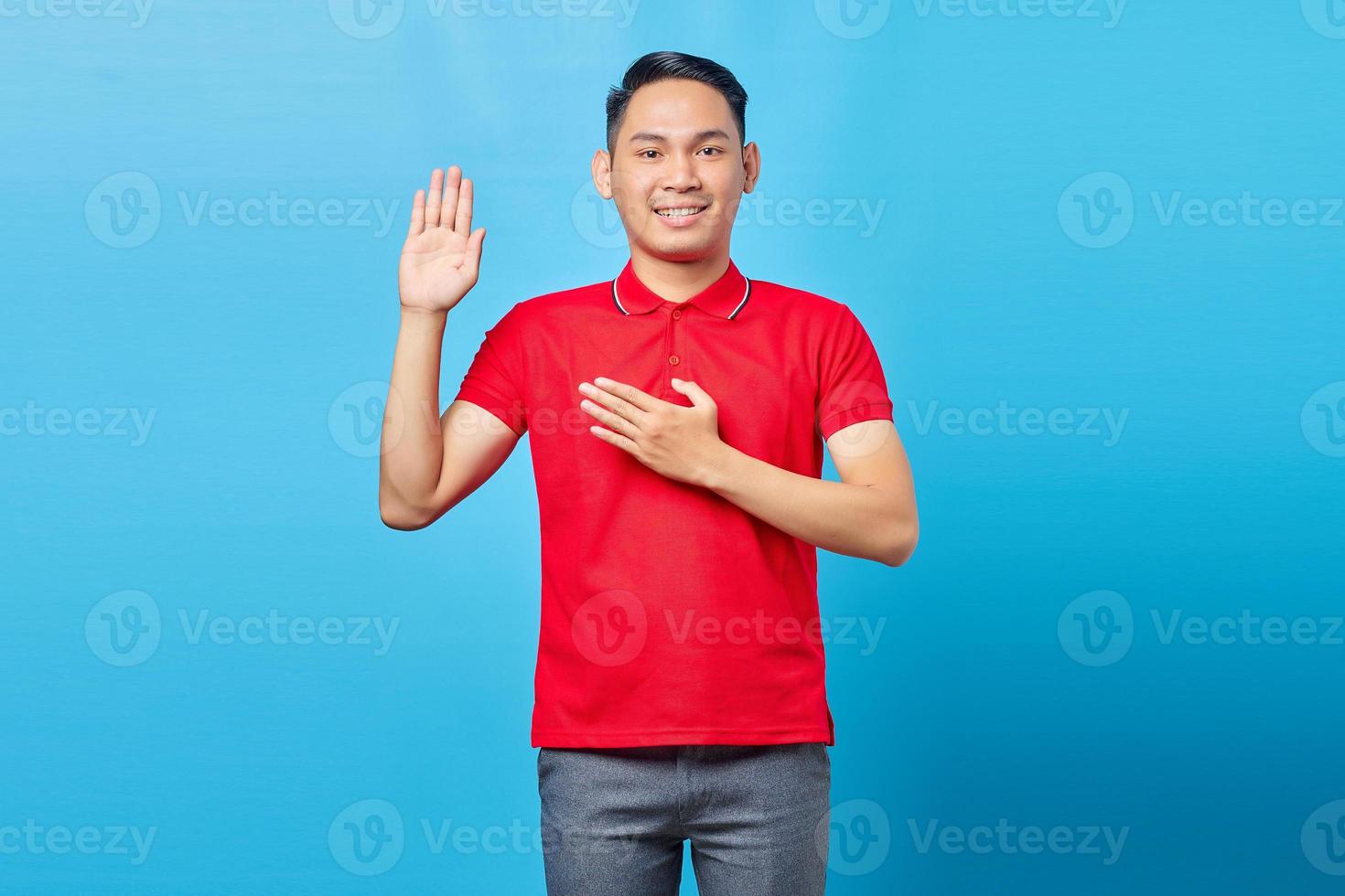 Portrait of handsome young Asian man smiling and showing greeting gesture towards isolated on blue background photo