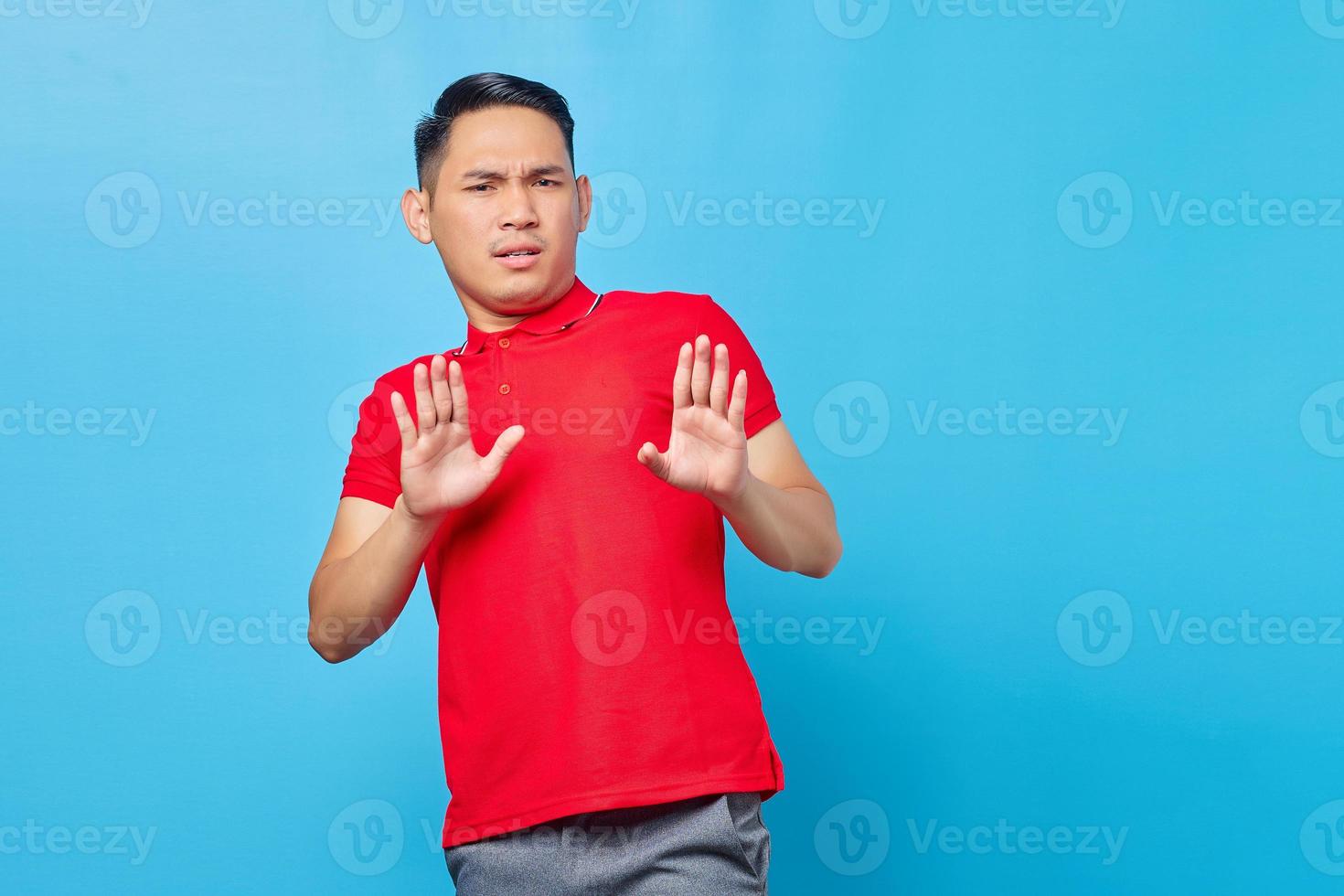 Retrato de hombre asiático joven molesto cruzando las manos hace gesto de parada, demuestra rechazo aislado sobre fondo azul. foto