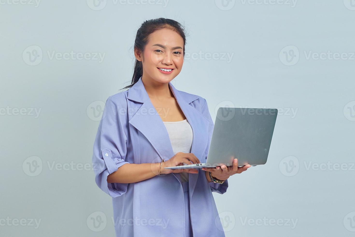 Portrait of smiling young Asian woman using laptop and looking at camera isolated on white background photo
