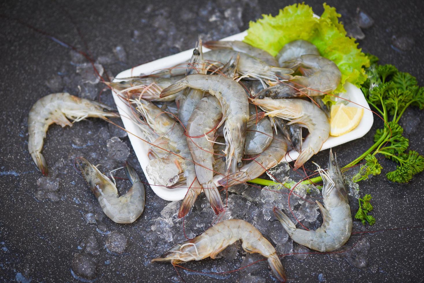 Fresh shrimp prawns for cooking with spices lemon on dark background in the seafood restaurant, raw shrimps on plate plastic tray, top view photo