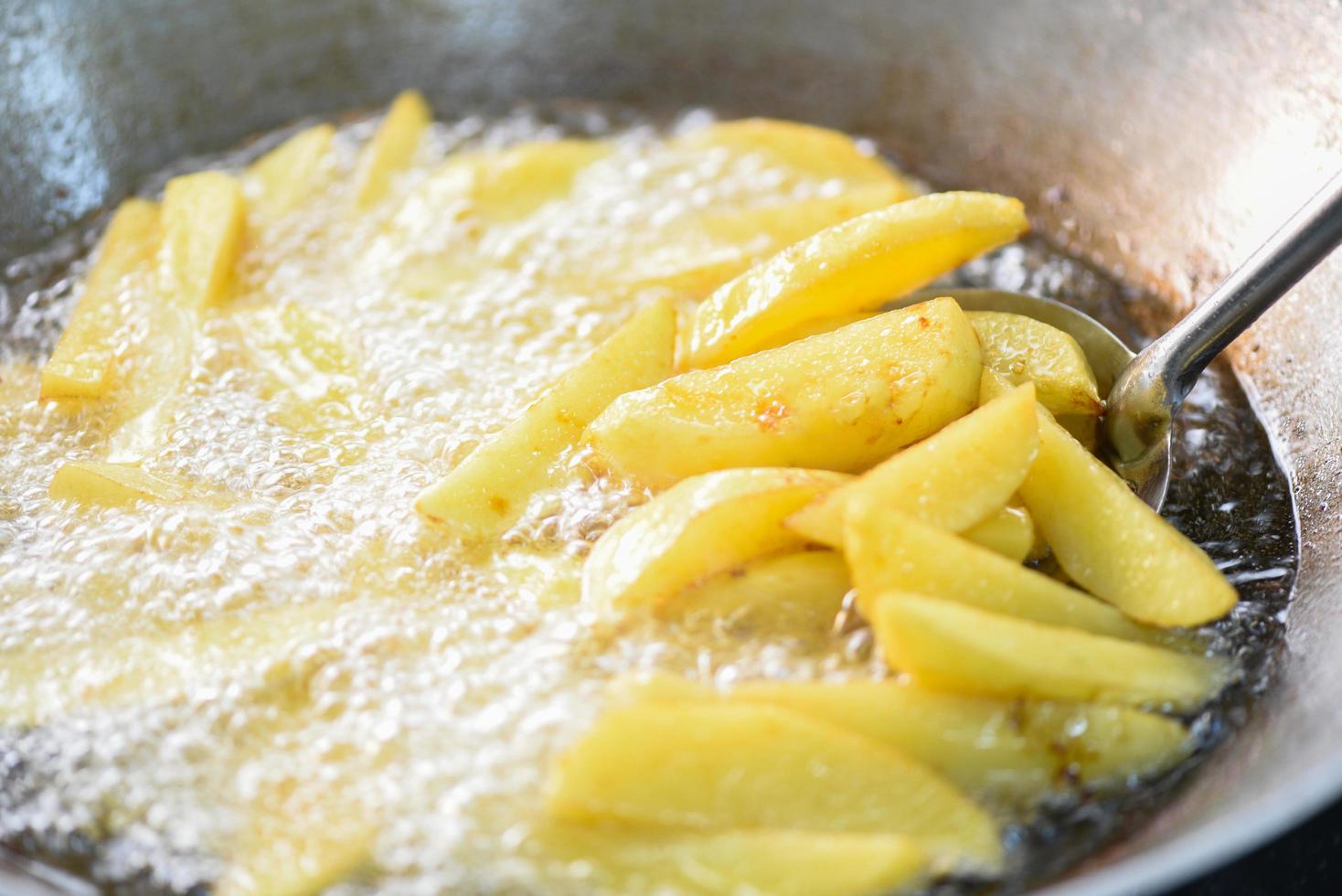 Cooking french fries or fry potatoes in hot oil for potato wedges, Close up fried potatoes in oil on pan photo