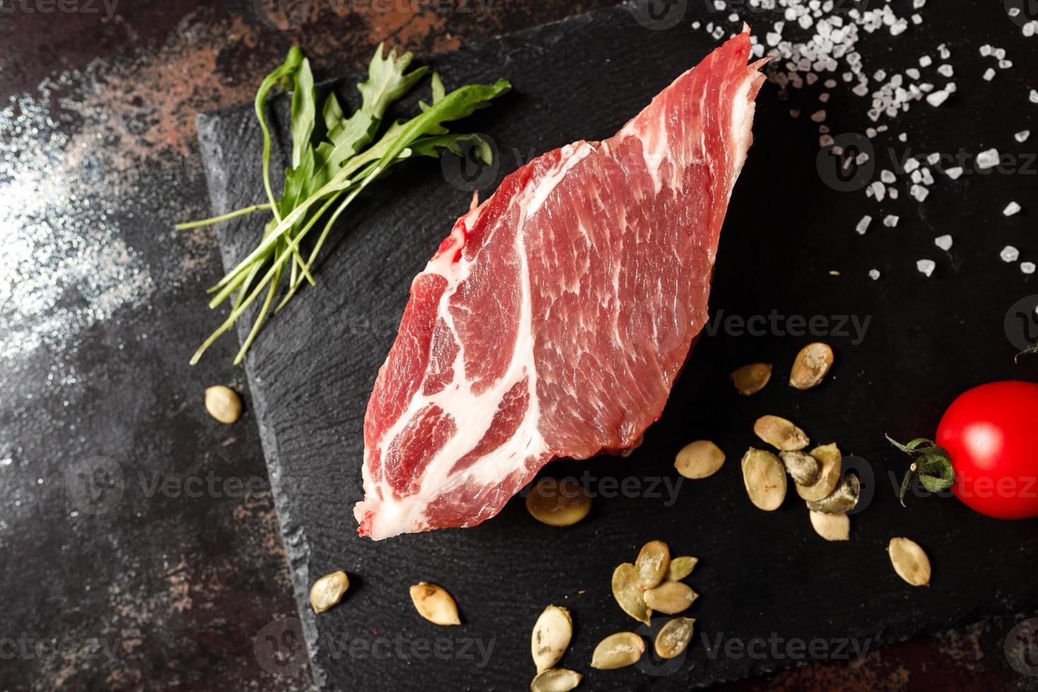 cerdo crudo con especias para cocinar al fuego o al horno sobre un fondo de piedra oscura foto