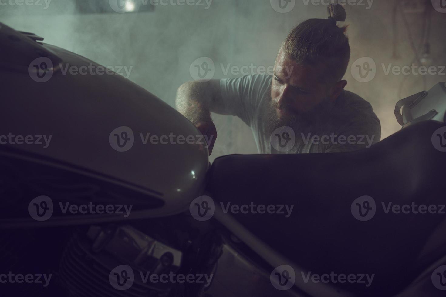un hombre guapo y brutal con barba reparando una motocicleta en su garaje foto