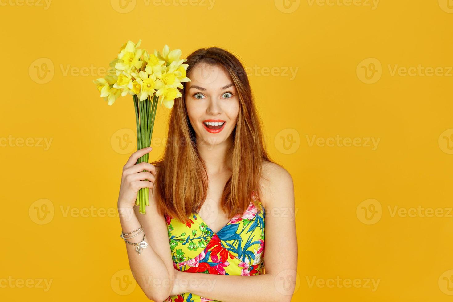 mujer sosteniendo flores amarillas y ella se sorprenderá contra la pared amarilla foto