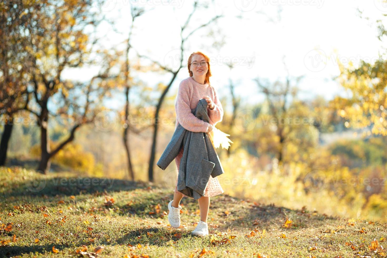 retratos de una encantadora chica pelirroja con una cara linda. chica posando en el parque de otoño con un suéter y una falda de color coral. la niña tiene un estado de ánimo maravilloso foto