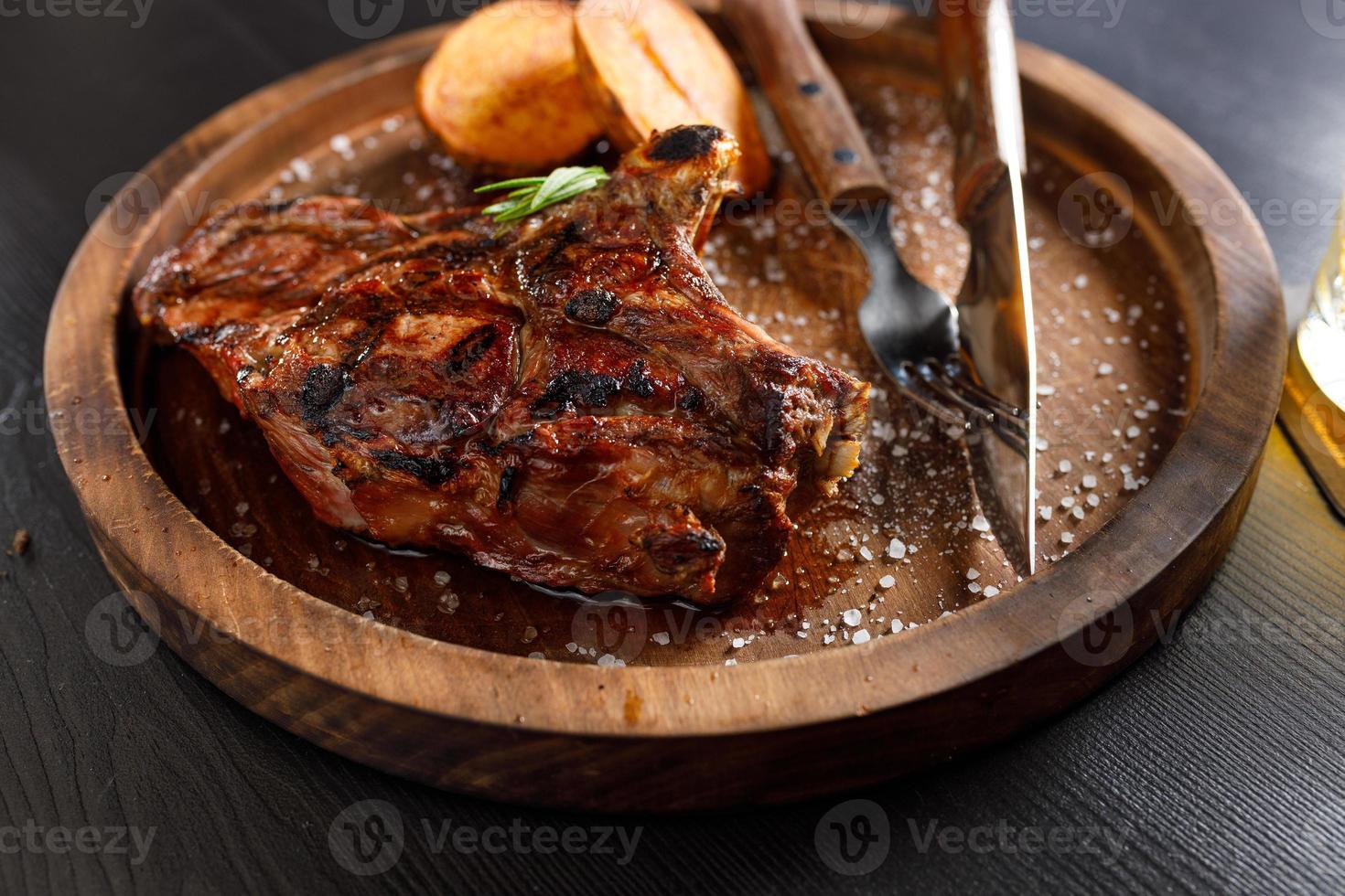 bistec medio raro sobre costilla de ternera con patatas en un plato de madera foto