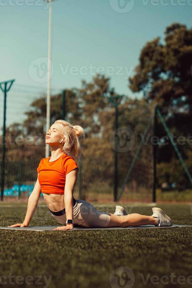 hermosa rubia haciendo estiramientos en el césped de un campo de fútbol foto