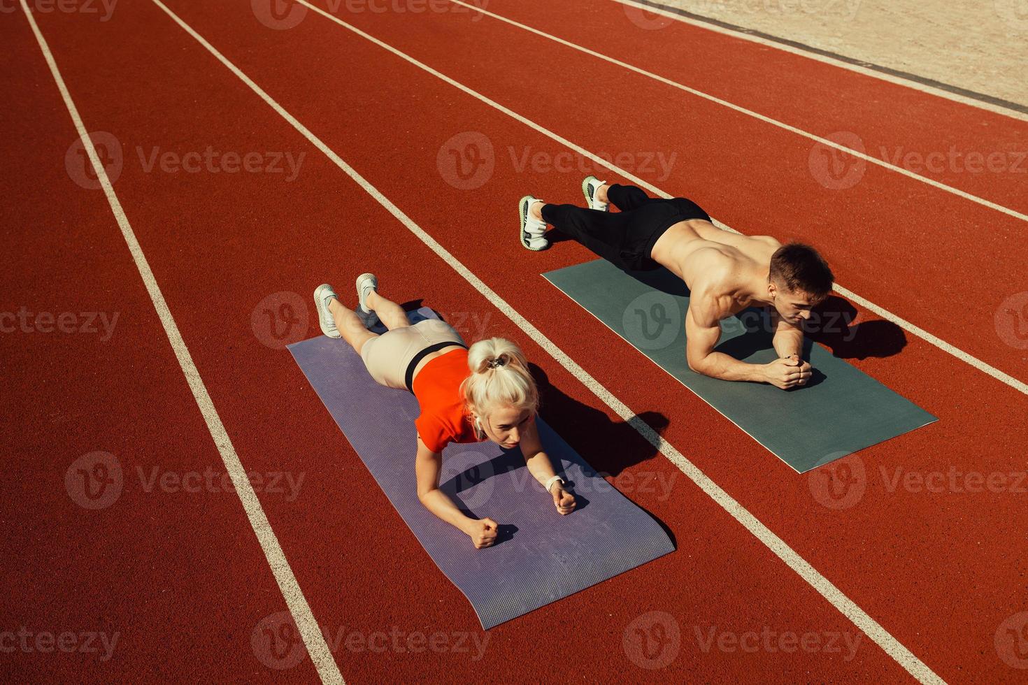 pareja joven haciendo deporte en el estadio acostado en colchonetas de yoga foto