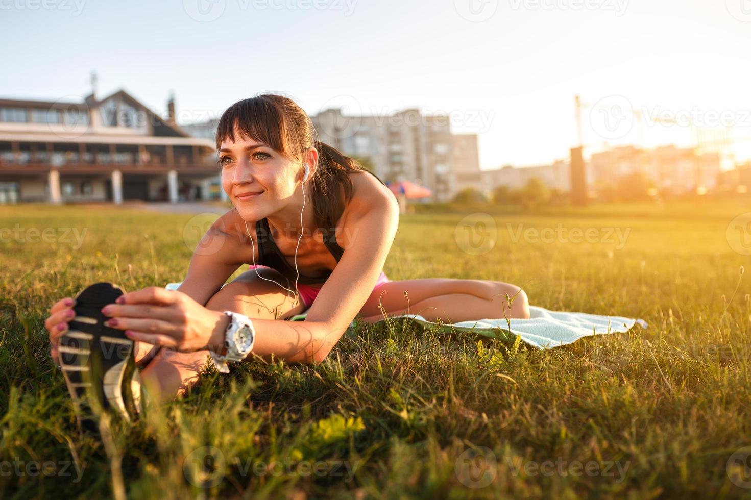 Athletic woman stretching her hamstring, legs exercise training fitness before workout outside with headphones listening music. photo