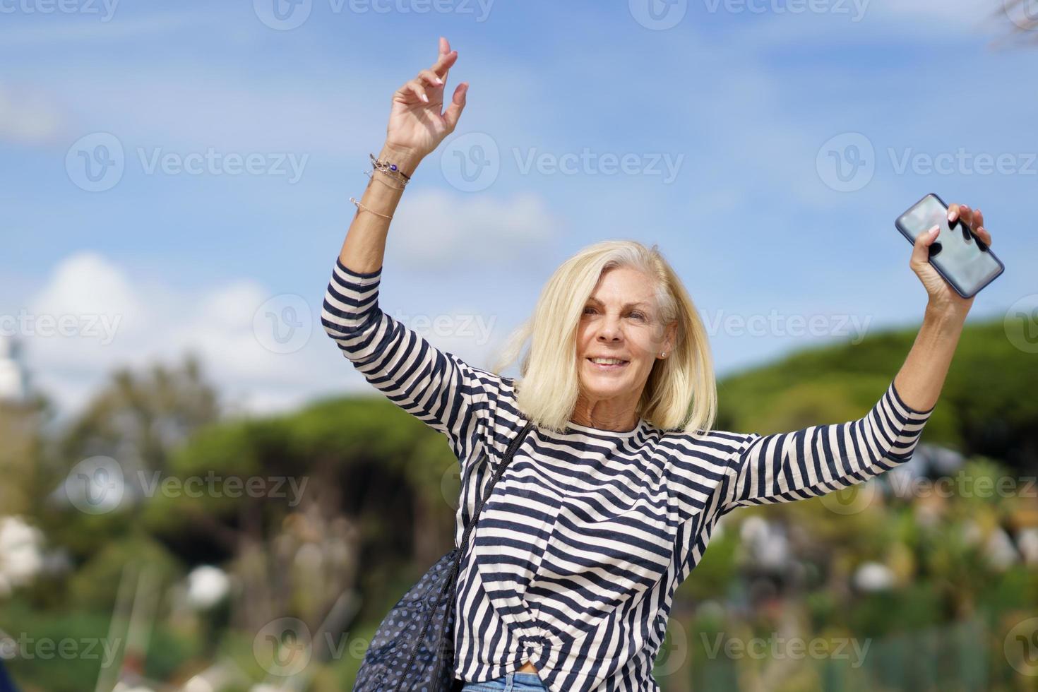 mujer madura paseando por un lugar junto al mar cerca de la playa, levantando los brazos con alegría. foto