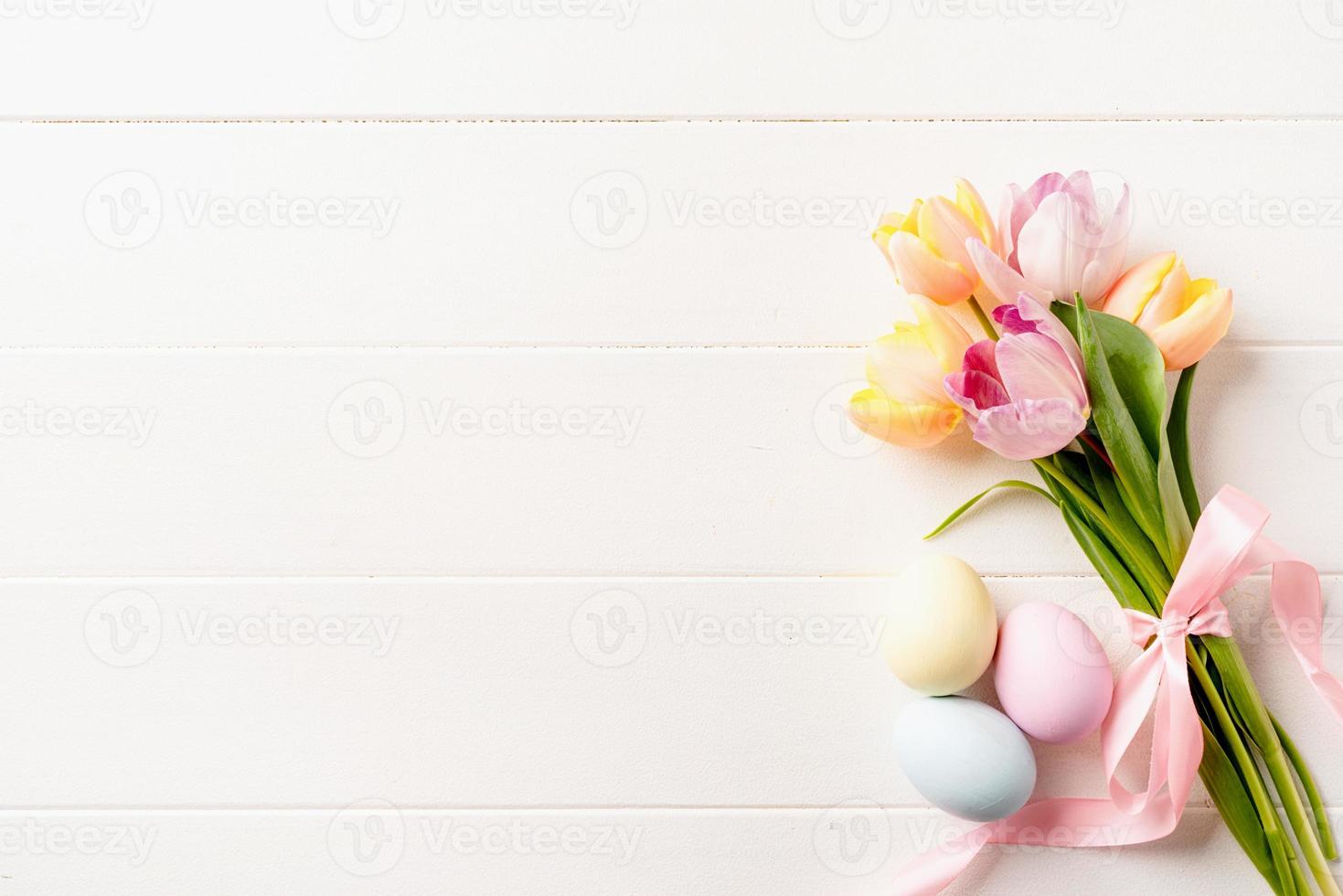 easter background with eggs and tulips on white wooden backdrop, top view flat lay photo