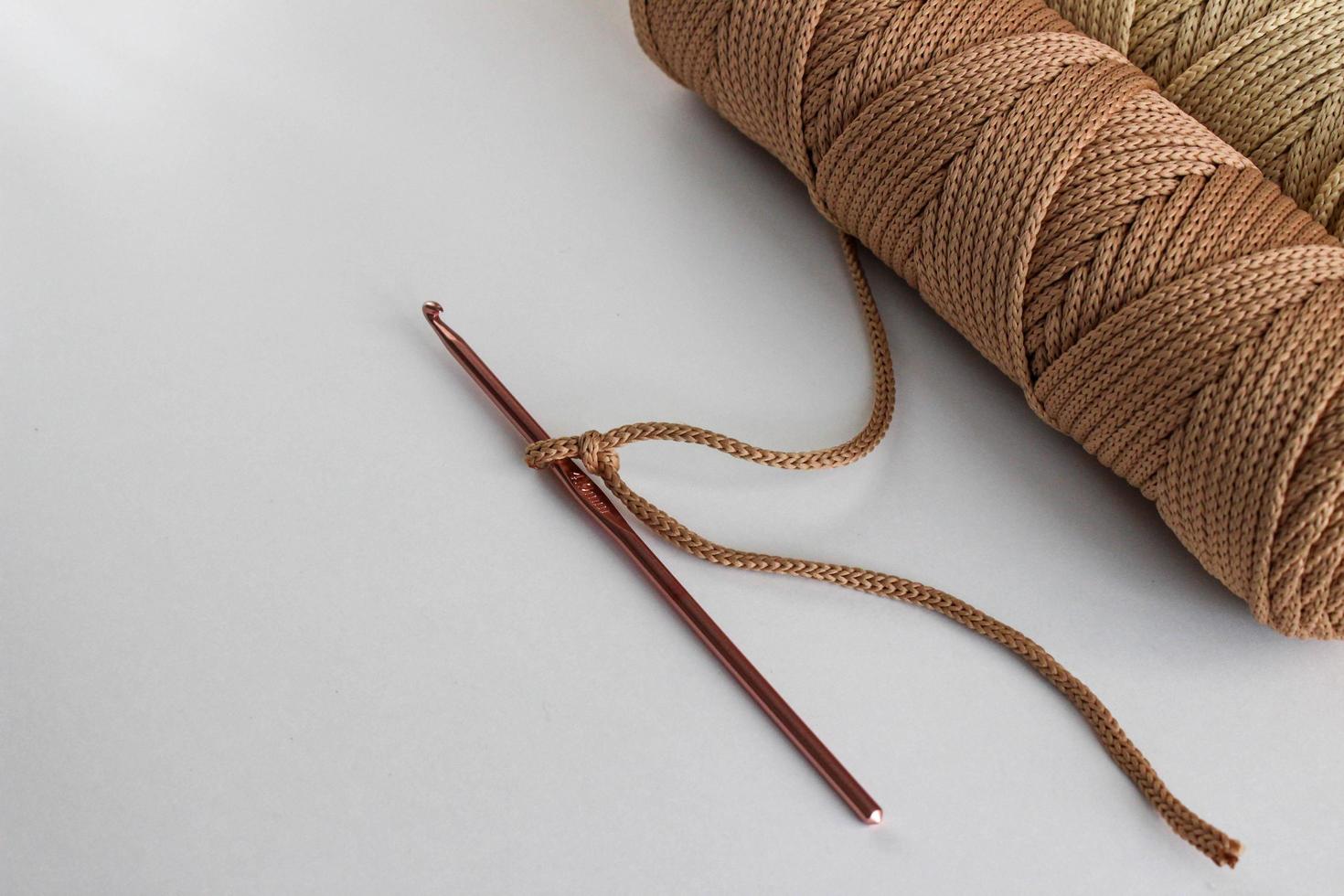 gancho de ganchillo beige y una madeja de cordón beige sobre un fondo blanco. en un gancho: un lazo del cordón, hecho para comenzar a tejer. tal cordón puede hacer una alfombra, un accesorio, etc. foto