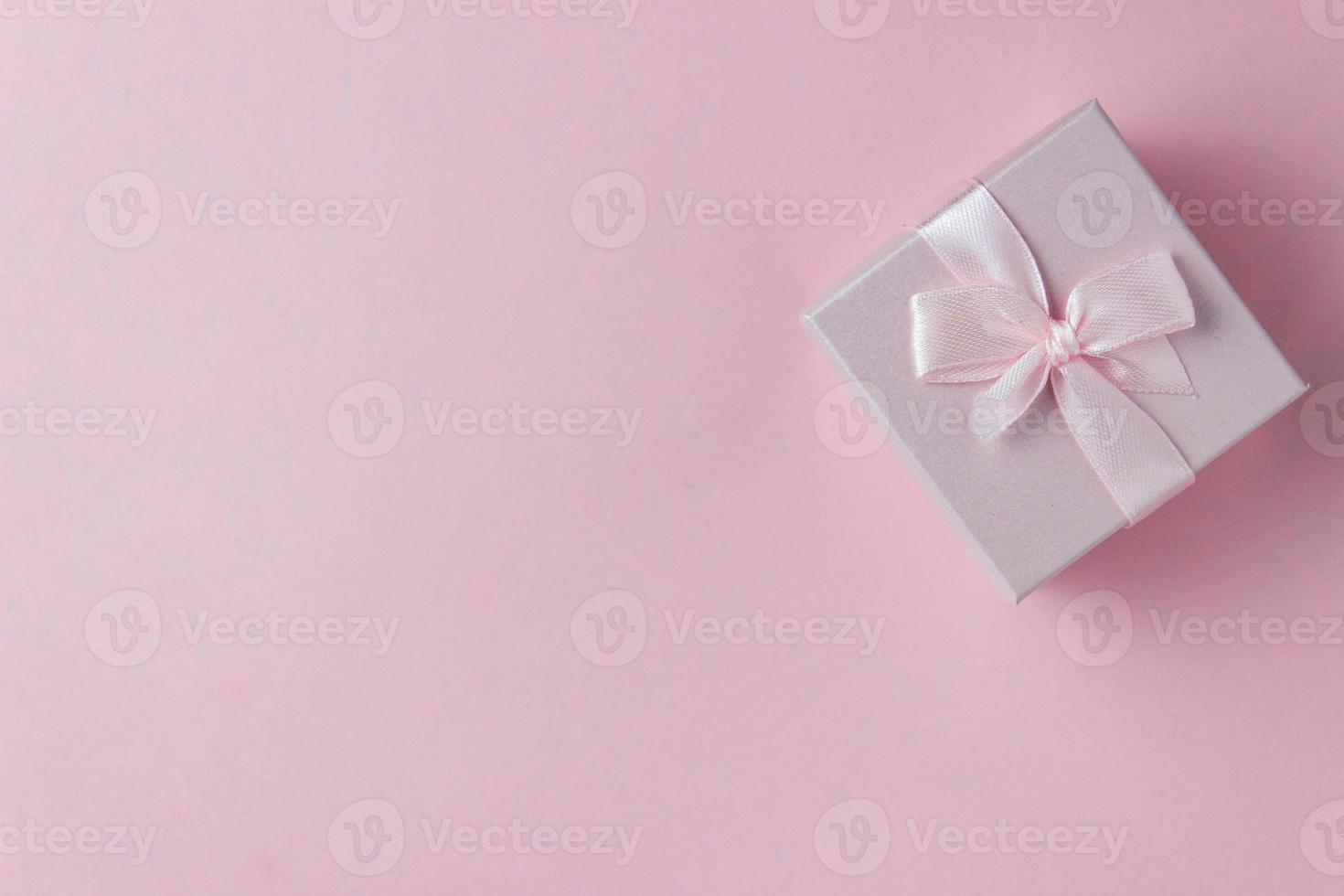 Pink gift box with ribbon tied bow on pink background. Top view photo