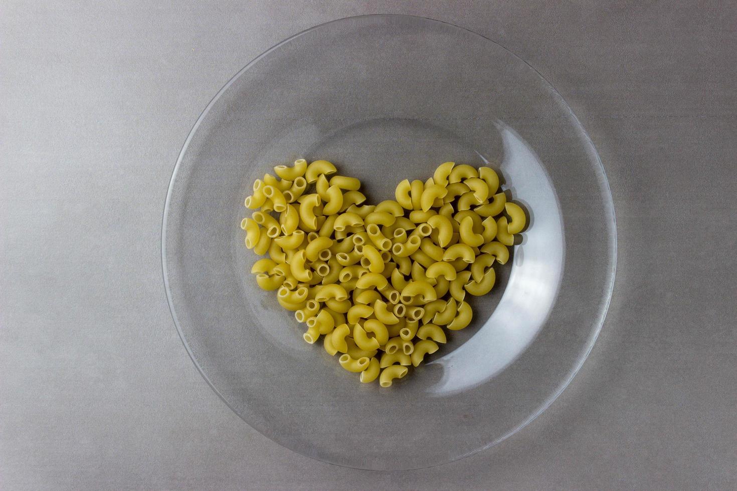 A handful of dry heart-shaped pasta on a transparent plate on a grey kitchen table photo