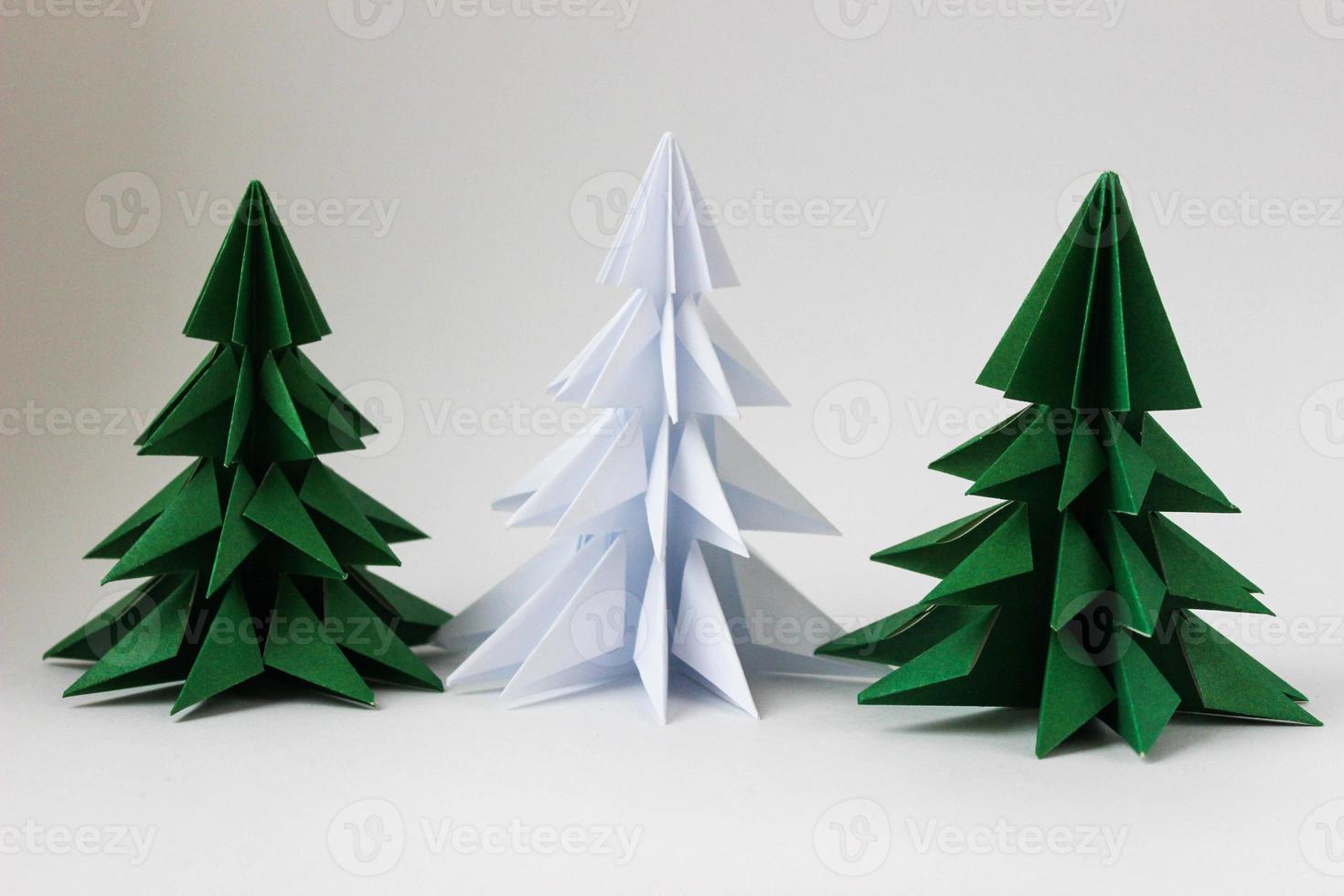 Two origami green christmas tree and white one on white background. photo