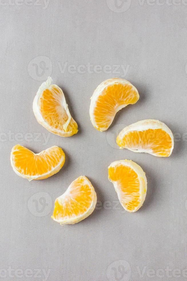 Mandarin slices laid out around in the shape of flower petals or sunlight on a gray background in the center of vertical photo