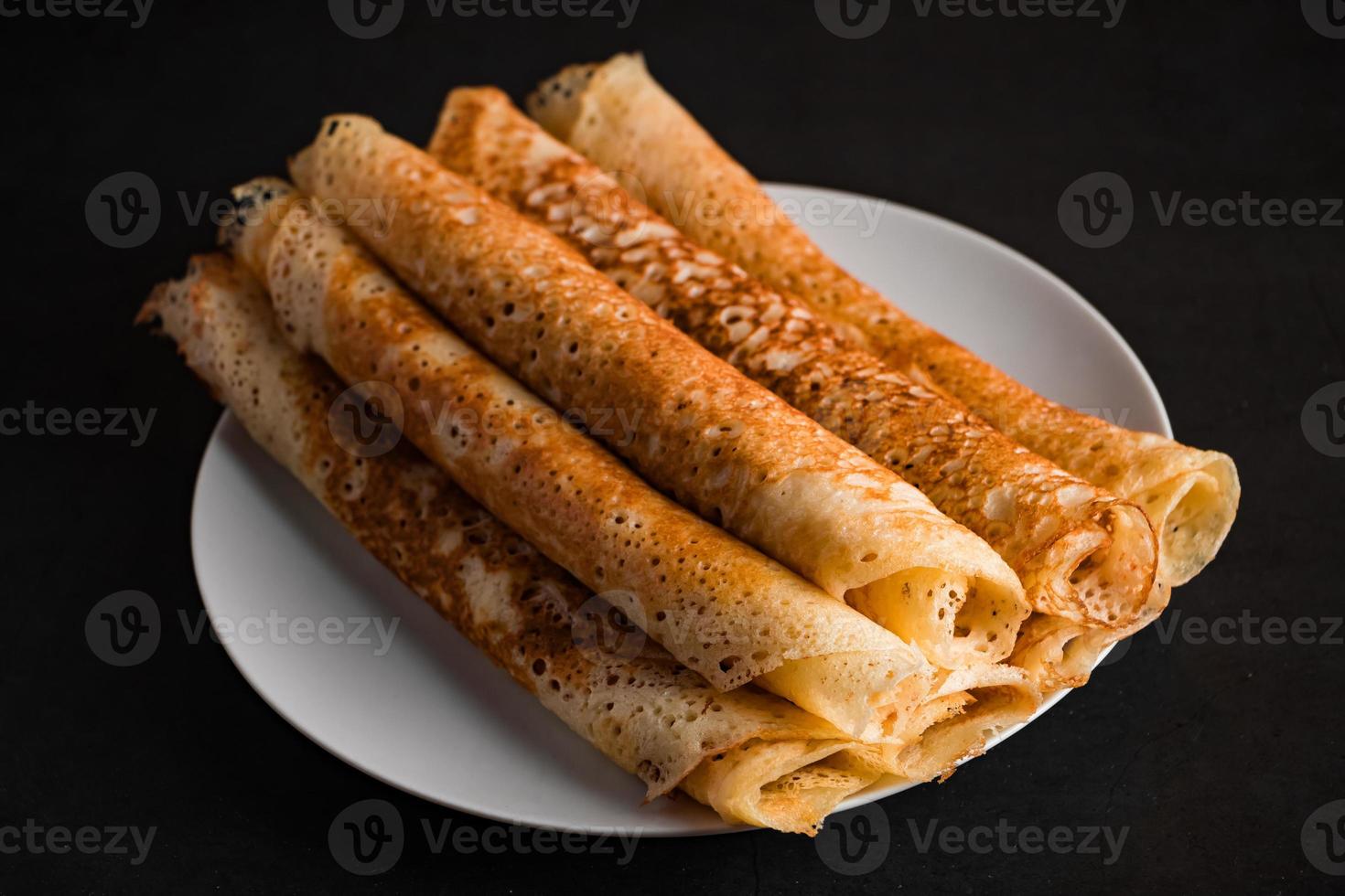 Tasty crepes on a plate on a black background. Traditional Russian food. photo